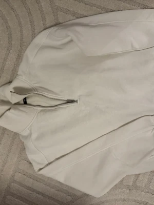 Vit hoodie med halv dragkedja 157 - Säljer en stilren vit hoodie från 157 med halv dragkedja framtill. Hoodien har en mjuk insida och klassisk huva. Perfekt för dig som gillar enkel och clean stil. Materialet känns tjockt och mysigt, perfekt för kyliga dagar.