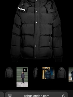 Svart pufferjacka från Gabos London - Säljer en svart pufferjacka från Gabos London med fet vaddering och hög krage. Jackan har huva, tryckknappar och dragkedja framtill samt Gabos-logga på kragen. Perfekt för kalla dagar och riktigt street. Jackan har elastiska muddar och en clean, oversized look. Jag säljer den nya som gabos london skickade till mig pga att min dragkjedja på jackan jag beställde därifrån gick sönder😊skriv för fler bilder med den på mig👍🏻