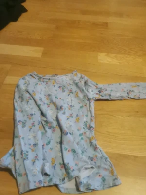 Blommig långärmad topp i ljusblått - Söt långärmad topp i ljusblått med blommigt mönster i flera färger. Toppen har rund halsringning och är tillverkad i ett mjukt, tunt material som känns skönt mot huden. Perfekt för dig som gillar en romantisk och lekfull stil.