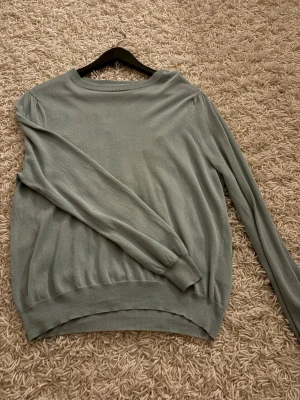 Ljusgrön stickad tröja från Ellos - Snygg ljusgrön stickad tröja från Ellos med rund halsringning och långa ärmar. Tröjan har ribbade muddar vid ärmslut och nederkant, vilket ger en klassisk och enkel look. Perfekt att matcha med jeans eller kjol för en avslappnad stil.