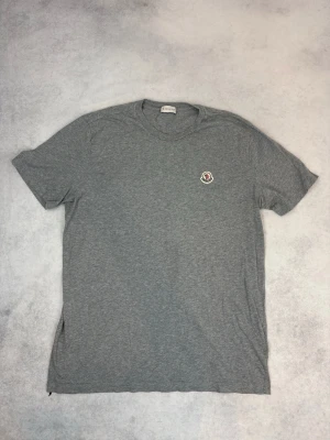 Grå Moncler t-shirt i bomull - Snygg grå t-shirt från Moncler med klassisk rund halsringning och liten Moncler-logga på bröstet. Tillverkad i mjuk bomull och har en normal passform med korta ärmar. Perfekt för en clean och stilren look.