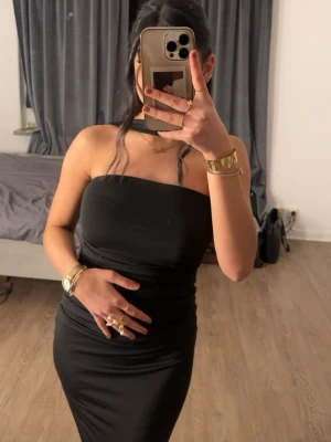 Svart långklänning - Snygg svart långklänning med axelbandslös design och figurnära passform. Klänningen har en stilren och enkel look som framhäver siluetten. Perfekt för dig som gillar minimalistisk stil och vill sticka ut med elegans. Är 160cm lång 