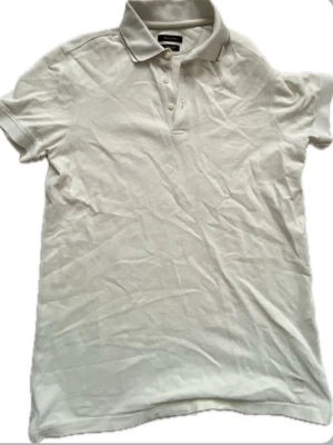 Vit pikétröja från Massimo dutti - Klassisk vit pikétröja från dutti med korta ärmar och krage. Tröjan har knappar vid halsen och är tillverkad i mjuk bomull som känns skön mot huden. Perfekt till jeans eller shorts för en clean och enkel stil.