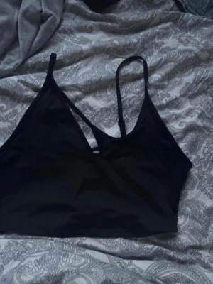 Svart bralette med asymmetriska band - Stilren svart bralette med tunna, asymmetriska axelband och mjuka triangelformade kupor. Perfekt för en trendig och bekväm look. Materialet ser ut att vara stretchigt och följsamt.För fler bilder/information skriv gärna, priset kan justeras 🤗❤️