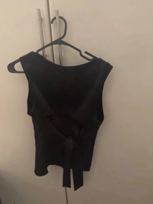 Svart ärmlös topp med knyt i ryggen - Snygg svart ärmlös topp med breda axelband och knytning i ryggen. Perfekt att styla med jeans eller kjol för en trendig look. Toppens material känns mjukt och följsamt mot kroppen. För mer bilder/justering av pris skriv gärna❤️🤗