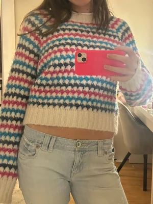 Flerfärgad randig stickadtröja  - Säljer en stickad tröja med breda ribbade muddar. Tröjan har ett färgglatt mönster. Mjuk och fluffig känsla, perfekt för dig som gillar en avslappnad men trendig stil.