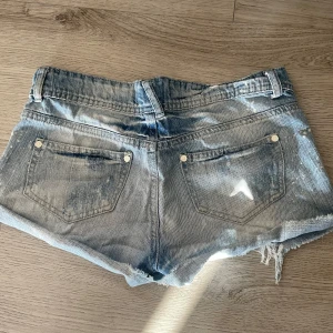 Blå jeansshorts med slitna detaljer - Snygga blå jeansshorts i storlek 34. De har fransiga och slitna kanter, klassisk femficksdesign och knappstängning. Perfekt för dig som gillar en avslappnad och cool stil med lite edge.
