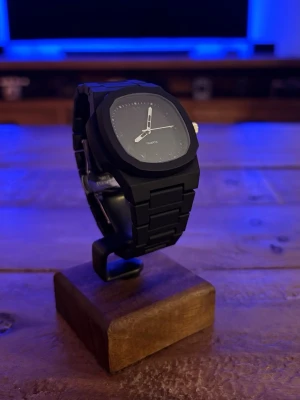 Svart stilren kvartsarmbandsklocka - Snygg svart armbandsklocka med kvartsurverk och minimalistisk design. Klockan har en matt svart länkarmband och svart urtavla utan siffror, vilket ger en clean och modern look. Perfekt accessoar för dig som gillar stilrena detaljer.