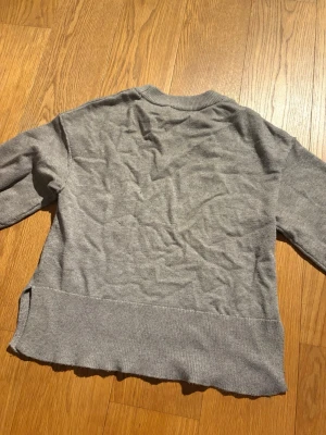 Grå stickad tröja från ginatrico - Mysig grå stickad tröja från ginatrico med rund halsringning och långa armar. Tröjan har ribbade muddar vid halsen och nederkanten samt en avslappnad passform. Perfekt att slänga på sig till jeans eller kjol.