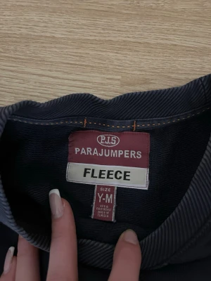 Mörkblå fleece från Parajumpers - Mörkblå fleece-tröja från Parajumpers med rund halsringning och ribbade muddar. Tröjan har ett stort gult tryck framtill och ett broderat PJS-märke på armen.