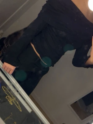 Svart offshoulder topp - Trendig svart klänning med offshoulder-design och lång ärm. Klänningen har en kroppsnära passform och en kort längd som ger en snygg siluett. Perfekt för dig som vill ha en stilren och modern look.