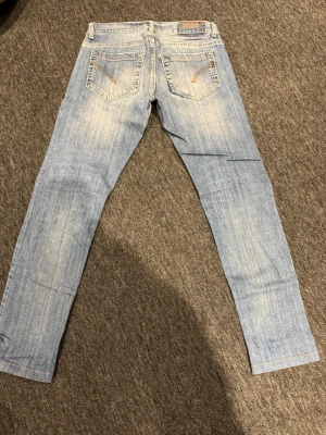 Ljusblå skinny jeans från Dondup - Säljer ett par ljusblå skinny jeans från Dondup med klassisk femficksdesign och snygga slitningar framtill. Jeansen har dragkedjedetaljer på bakfickorna och är tillverkade i mjuk denim med en smal passform. Perfekta för en avslappnad och trendig look.