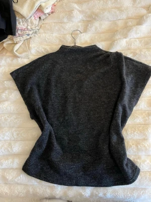 Mörkgrå stickad väst - Mysig mörkgrå stickad väst med breda, korta ärmar. Perfekt att slänga över en tröja för extra värme. Super skön och ej ”stickig” i materialet