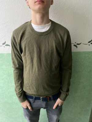 Olivgrön tröja från Riley - Säljer en stilren olivgrön tröja från Riley med rund halsringning och långa ärmar. Tröjan är tillverkad i ett tunt, mjukt material och har ribbade muddar vid ärmslut och nederkant. Perfekt att matcha med jeans eller chinos.