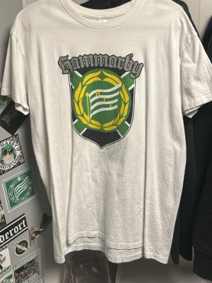 Vit Hammarby t-shirt från SOL'S - Vit t-shirt från SOL'S med stort Hammarby-tryck på bröstet i grönt, gult och svart. Klassisk rund hals och korta ärmar. Tillverkad i mjuk bomull, perfekt för dig som vill visa ditt stöd för Hammarby på ett stilrent sätt.