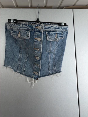 Kort jeantoppfrån FB Sister - Säljer en snygg kort jeanstopp från FB Sister i blå denim med fransig kant och knappar framtill. Storlek L men sitter som en S