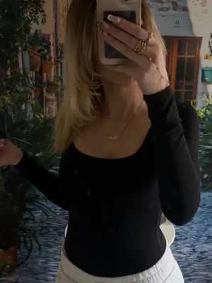 Långarmad body - Snygg svart långärmad topp med rundad halsringning och tight passform. Perfekt att styla med både jeans och kjol för en trendig look. Enkel och stilren design utan synliga detaljer eller mönster.