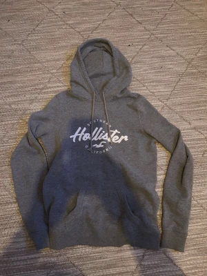 Vintage Hollister hoodie - Snygg grå hoodie från Hollister, tröjan är vintage som är eftertraktat. Skicket är 10/10 och tecken på användning finns inte. Storleken är M men passar även S. Startpriset är 599 men kan diskuteras😊😊