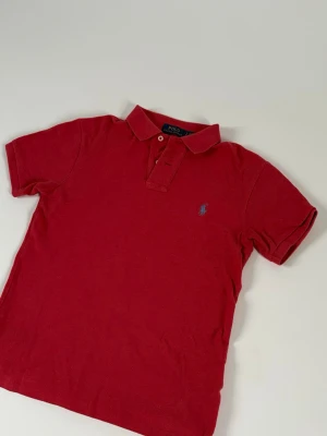 Polo Ralph Lauren  - Snygg röd pikétröja från Polo Ralph Lauren med klassisk krage och två knappar framtill. Hör av dig vid frågor. Den sitter som XS