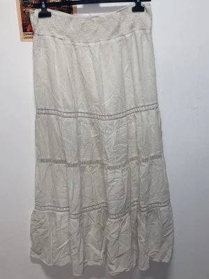 Vit långkjol från Indiska - Lång, vit kjol från Indiska med bred och bekväm resår i midjan + volangdetaljer. Fin att ha både hög och lågmidjat. Kjolen har en luftig och flowy känsla, perfekt för sommaren. Som sista bilden visar så har kjolen två lager, alltså inte genomskinlig.