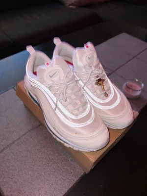 Nike Air Max 97 vita sneakers - Säljer ett par fräscha Nike Air Max 97 sneakers i helvitt med reflekterande detaljer och röda inslag på insidan. Skorna har den ikoniska vågiga designen, synlig Air-sula och är gjorda i mesh och syntetmaterial. Perfekta för dig som vill ha en clean och sportig look. 