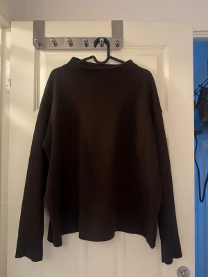 Mörkbrun stickad tröja - En enkel och stilren mörkbrun stickad tröja med lång ärm och rak passform. Tröjan har en rund halsringning och är gjord i ett mjukt stickat material som passar perfekt för kyliga dagar. Inga synliga detaljer eller mönster, bara klassisk och clean design.