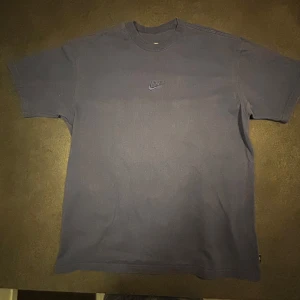Blå Nike t-shirt med logga - En stilren blå t-shirt från Nike med liten broderad logga på bröstet. Klassisk rund halsringning och korta ärmar. Perfekt till jeans eller shorts för en avslappnad look. Loose fit medium herr. Säljs i befintligt skick, knappt använd.