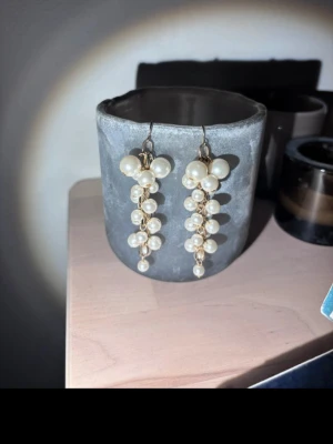 Guldplätterade Hängande örhängen med pärlor - Säljer ett par eleganta hängande örhängen med vita pärlor i olika storlekar. Örhängena har en guldig metallbas och pärlorna är arrangerade i en klusterdesign som ger ett lyxigt intryck. Perfekta för dig som vill ha något extra till din stil. (Alla smycken kommer i askar)