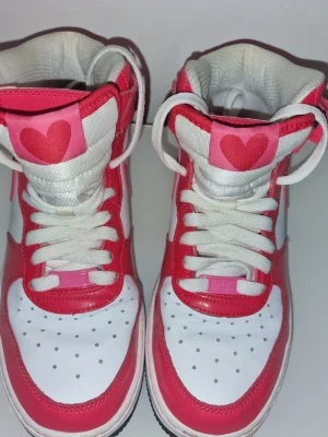 Vita och rosa high-top sneakers med hjärta - Unika high-top sneakers i vitt och rosa med ett stort rött hjärta på tungan. Perfekt för dig som vill sticka ut med en lekfull och färgglad stil. Använd 1 gång och finns ej att köpa längre 🩷