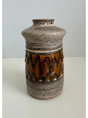 Retro keramikvas med zigzag-mönster - Säljer en retro keramikvas i brunt och beige med tydligt zigzag-mönster runt mitten. Vasen har en rustik yta och bred öppning upptill. Perfekt som inredningsdetalj för dig som gillar vintage och unika former. Mycket gott skick. 