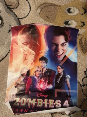 Disney Zombies 4 affisch - Säljer en färgstark affisch från filmen Disney Zombies 4: Dawn of the Dead. Affischen har motiv med flera karaktärer och coola effekter i rött, blått och svart. Perfekt för dig som gillar Disney Channel och zombies-tema.