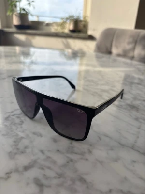 Svarta QUAY Nightfall solglasögon - Säljer ett par svarta QUAY Nightfall solglasögon med rektangulär, oversized sköldformad båge och mörka tonade linser. Snygg och modern design med QUAY-logga på skalmen. Perfekta för dig som vill sticka ut med en trendig accessoar.