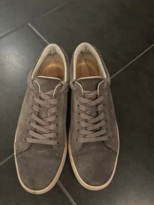 Gråa Vagabond skor - Snygga sneakers i grå mocka med matchande grå skosnören och beige yttersula. Klassisk låg modell med enkel design som passar till det mesta. Insidan är ljus och skon har en stilren look utan synliga loggor.
