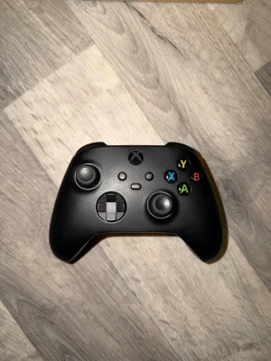 Svart Xbox Series X/S handkontroll. OBS! Med stickdrift. - Snygg svart Xbox Series X handkontroll med klassisk layout, två analoga spakar(OBS! En av spakarna har stickdirft), styrkors och färgade ABXY-knappar. Ergonomisk design i matt plast som ligger skönt i handen. Kompatibel med: Xbox Series X/S, Windows 10/11, Android, iOS. 3,5 mm uttag för headset. Med denna kontrollen ingår det två nya Energy+ AA 1,5V batterier.