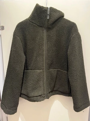 Grön Teddy jacka från H&M i storlek M - Grön Teddy jacka från H&M i storlek M. Jacka är i ett otroligt bra skick och har inga defekter! Jackan säljs inte heller längre så ganska svår och få tag på! 