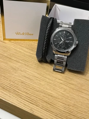 Regal Klocka - 45mm (med box) - Säljer en snygg Regal herrklocka i rostfritt stål med svart urtavla och stilrena detaljer. Perfekt både till vardag och mer uppklädda tillfällen. Tidlös design som passar alla outfits.  Detaljer: 	•	Märke: Regal (köpt på Ur & Penn) 	•	Svart urtavla med kronograf-detaljer 	•	Rostfritt stål 	•	Japan quartz-urverk 	•	Justerbart armband (extra länkbitar medföljer) 	•	Originalbox ingår  Skick: Bra skick, fungerar som den ska Batteridriven   Hör av dig vid frågor eller bud! 