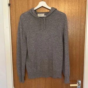 Grå kashmirhoodie från Sayless - Mjuk och stilren grå hoodie från Sayless i lyxig kashmir. Tröjan har huva med snörning och långa ärmar, perfekt för dig som gillar en chill och clean look. Passar dig som vill ha något både bekvämt och snyggt till vardags. 