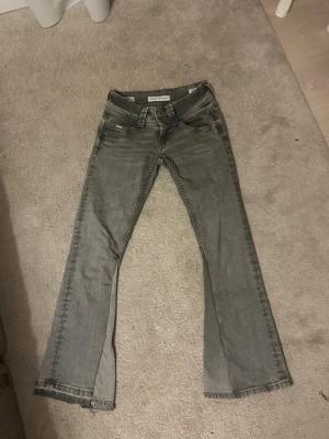 Grå bootcut jeans från Gina Tricot - Snygga grå jeans från Gina Tricot med bootcut-modell och klassisk femficksdesign. Jeansen har låg midja och är tillverkade i stretchigt denimtyg för skön passform. Perfekta för dig som gillar en avslappnad men trendig look. Omsydda ! 