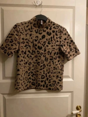 Leopardmönstrad blus från Hailys - Snygg leopardmönstrad blus från Hailys i beige och svart med bruna detaljer. Blusen har korta ärmar och rak passform. Materialet känns mjukt och lite tjockare, perfekt för dig som vill sticka ut med ett djurmönster.