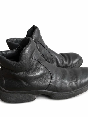 Svarta läderstövletter från Ecco storlek 38 - Säljer ett par svarta stövletter från Ecco i mjukt, äkta läder. Skorna har en rundad tå, diskret dragkedja på sidan och en bekväm, vadderad kant runt ankeln. Sulan är robust och ger bra grepp. Perfekta för dig som gillar stilrena boots med en klassisk look.