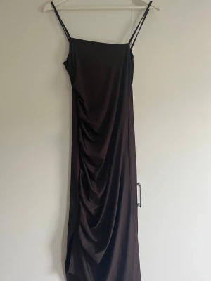 Brun långklänning med drapering - Snygg brun långklänning med smala axelband och draperad effekt längs sidan. 