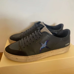 Mörkblå sneakers från Axel Arigato - Snygga mörkblå sneakers från Axel Arigato med broderad fågel, nypris 2300 kr. Den har flera små defekter men inget man ser på håll. Kommer med skolåda, påse och rengörings servetter. Påsen har klistermärken på baksidan.