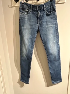 Blå slim fit jeans - Säljer ett par polo ralph lauren blå slim jeans. Jeansen är slim fit och har stretchigt denimtyg för extra komfort.  Litet hål i jeansen enligt bild