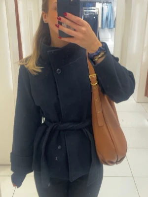 Mörkblå kort kappa med knytskärp - Snygg mörkblå kort kappa med hög button up krage och knytskärp i midjan. Från Ginas Young kollektion, 158/164 men passar mig perfekt som har S. Snygg jacka till våren. Använd max några gånger. 
