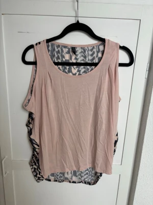 Beige och svart mönstrad linnetopp - Säljer en cool ärmlös linnetopp i beige med svart mönstrad baksida. Toppen har rund halsringning och ett avslappnat, loose fit. Perfekt för dig som gillar unika detaljer och vill sticka ut lite extra.