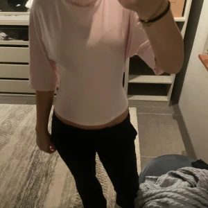 Ljusrosa omlottopp med knyt i ryggen - Säljer en ljusrosa omlottopp med trekvartsärm och snygg knytning i ryggen. Toppen är croppad och har en mjuk, stretchig känsla. Perfekt för dig som gillar en feminin och trendig look. 