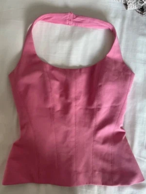 Rosa korsettopp med halterneck - Trendig rosa korsettopp med halterneck och markerade sömmar framtill. Toppen har en figurnära passform och är perfekt för att skapa en snygg siluett. Passar till både jeans och kjol för en cool look.