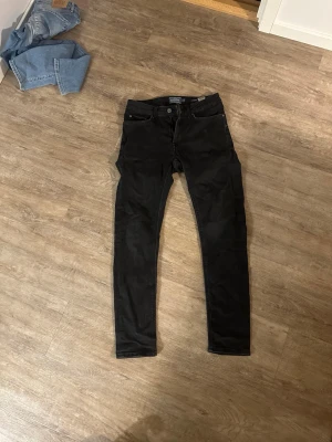 Svarta slim fit jeans från Jack & Jones - Snygga svarta slim fit jeans från Dressman med klassisk femficksdesign och normal midja. Jeansen har en stilren look och är perfekta för en trendig vardagsstil. Materialet är mjukt och stretchigt för extra komfort.