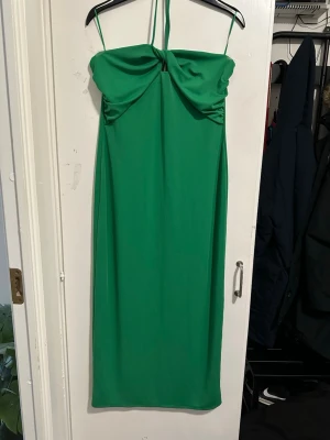 Grön axelbandslös klänning strl: M/L - Snygg grön axelbandslös klänning med knutdetalj framtill och smala axelband. Klänningen har en rak passform och är perfekt för dig som vill sticka ut med en färgstark look. Materialet känns mjukt och följsamt.