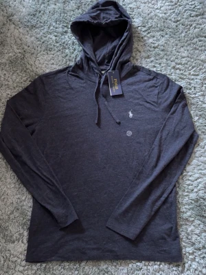 Ralph lauren hoodie - Snygg svart hoodie från Polo Ralph Lauren med klassisk huva och dragsko. Liten broderad logga på bröstet och mjukt, tunt material som känns skönt mot huden. Perfekt för en avslappnad och stilren look.